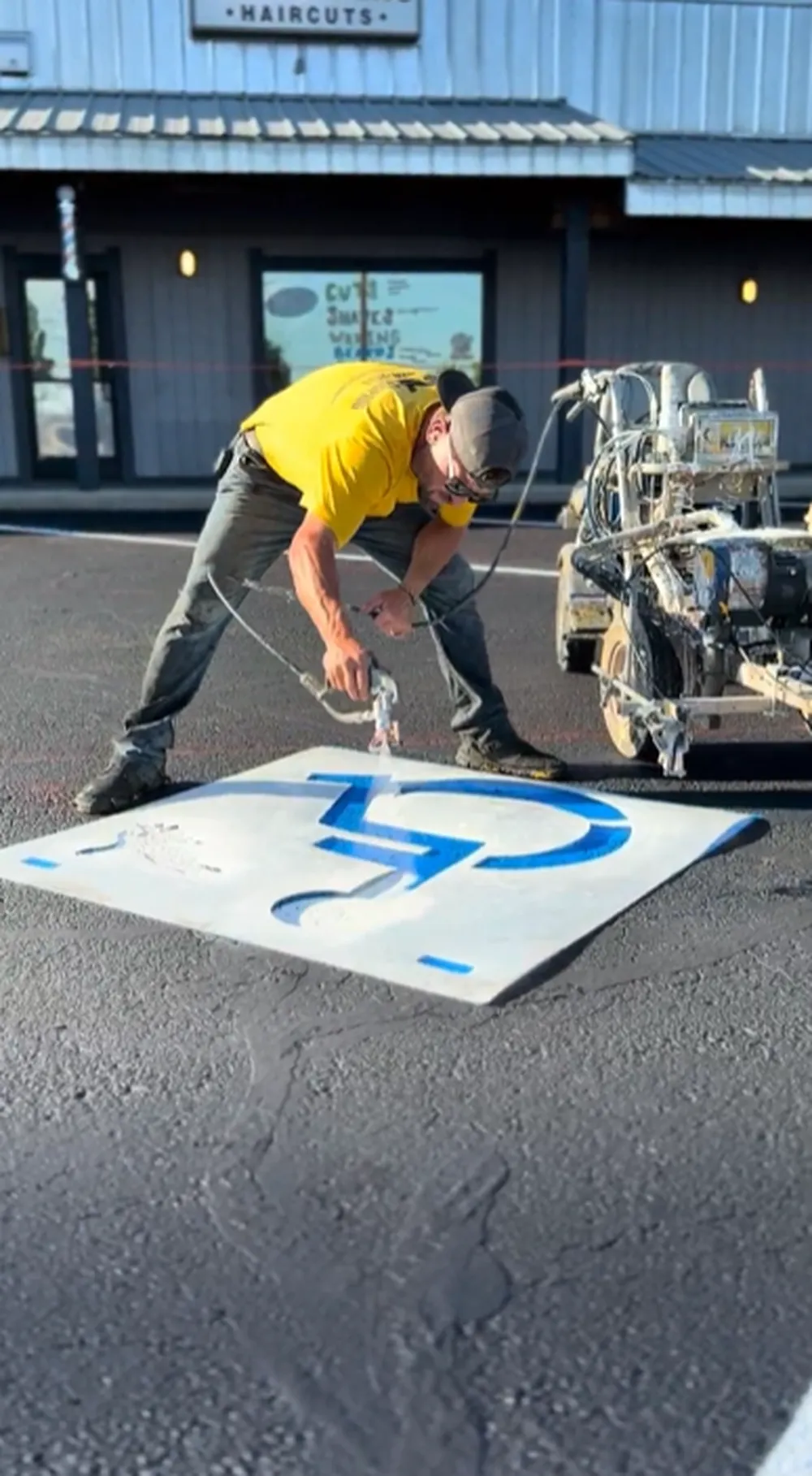 Superior Striping technician spray painting a blue ADA wheelchair handicap symbol stencil on a freshly sealcoated parking lot in Boise, Idaho