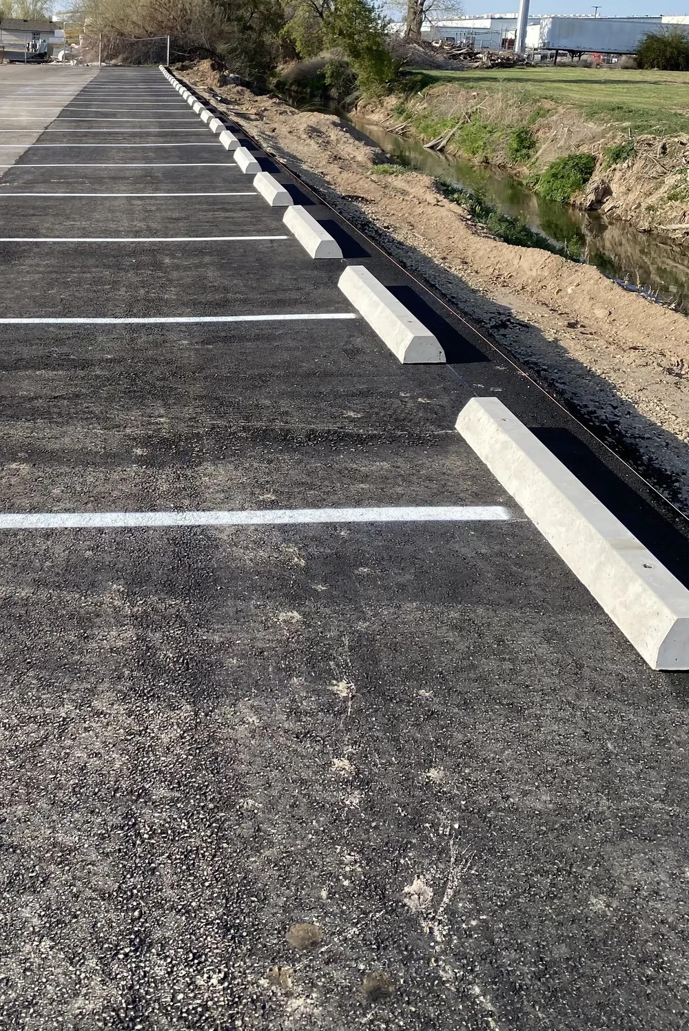 A long row of new concrete parking blocks and freshly painted white parking stall lines on a commercial asphalt lot in Treasure Valley by Superior Striping.