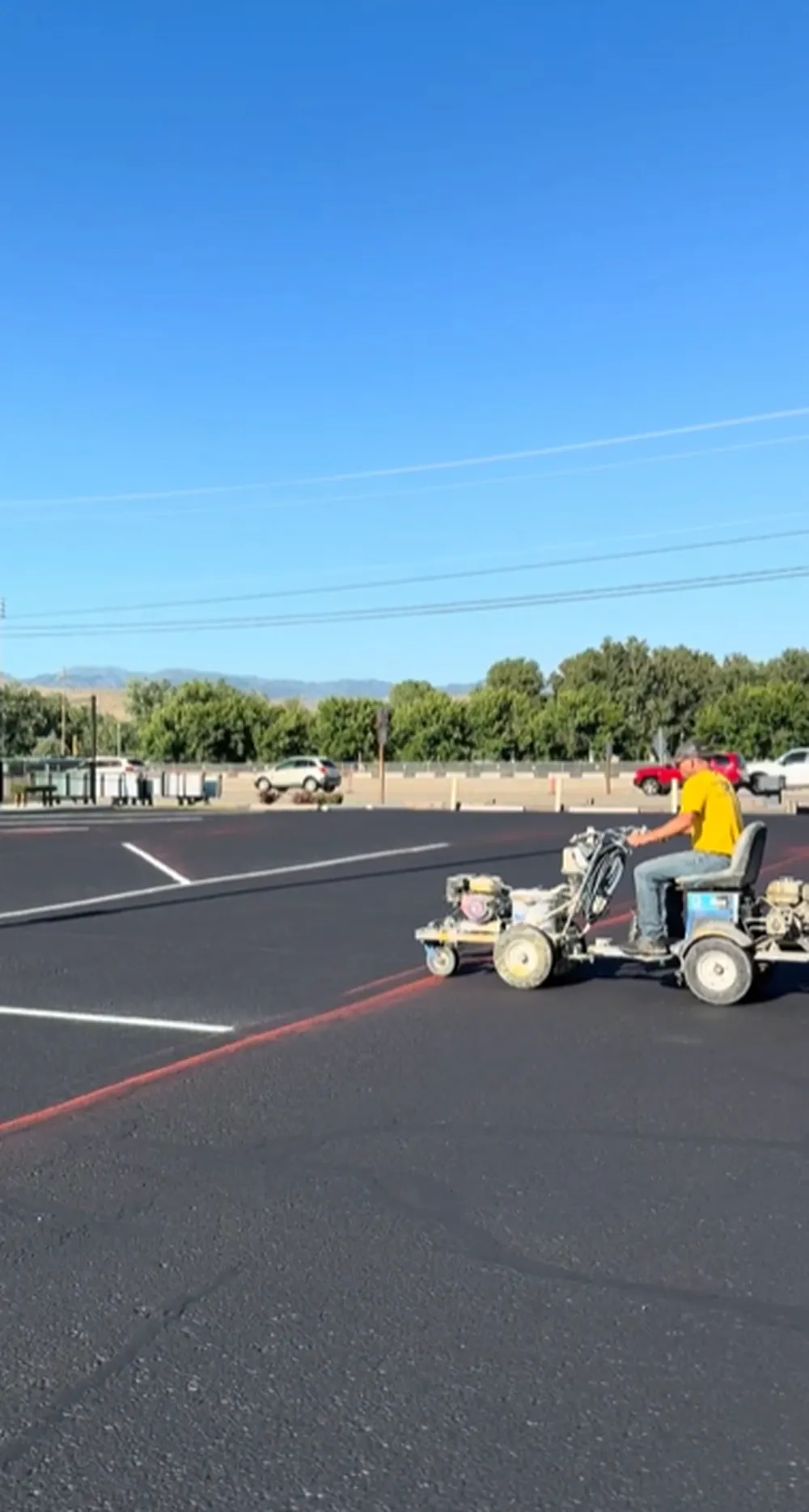 Superior Striping technician riding a line striping machine across a freshly sealcoated parking lot with Boise, Idaho mountains in the background