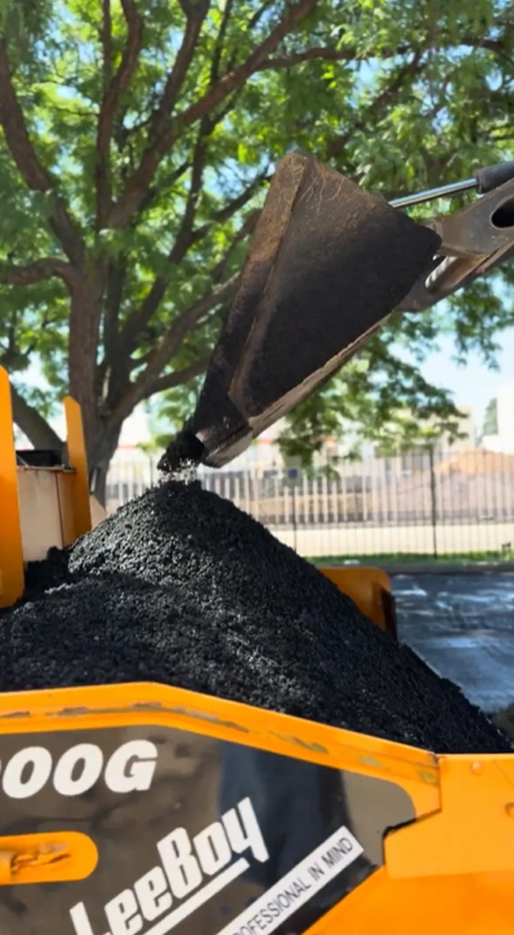 Skid Steer Bucket Dumping Hot Mix Asphalt Into Leeboy 1000G Paver Hopper During Parking Lot Replacement in Boise, Idaho