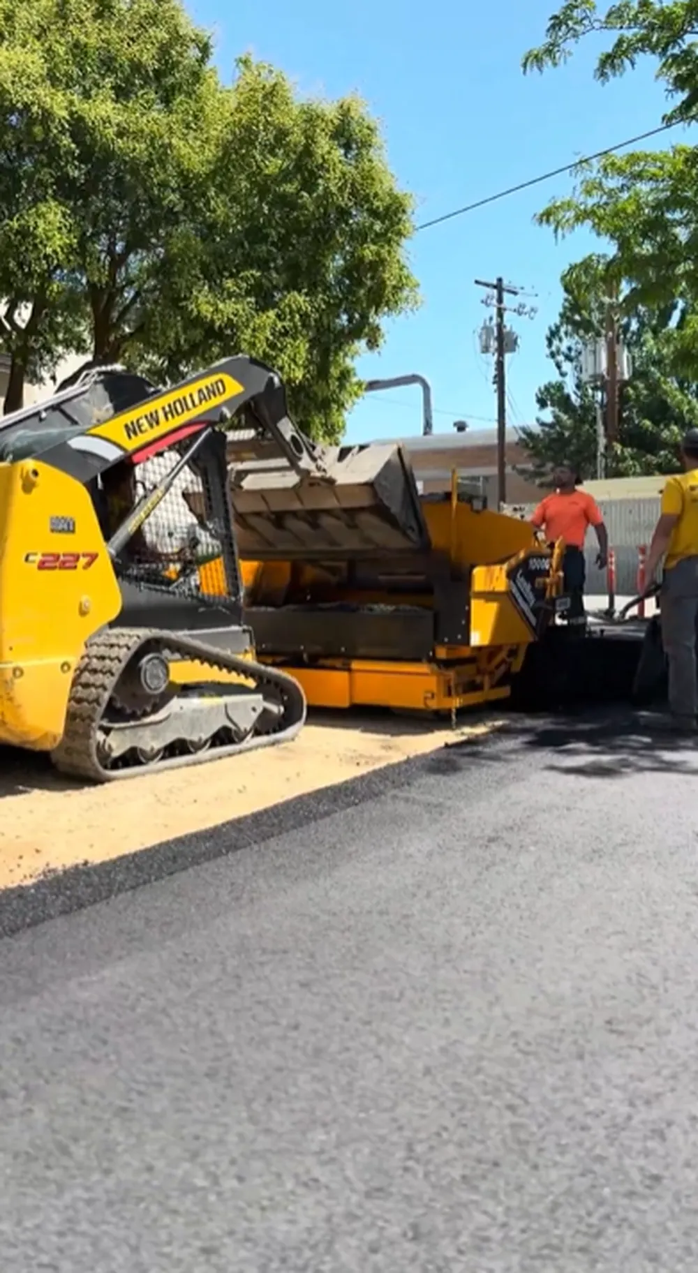 New Holland Skid Steer Feeding Asphalt Into Leeboy Paver During Parking Lot Replacement in Boise, Idaho