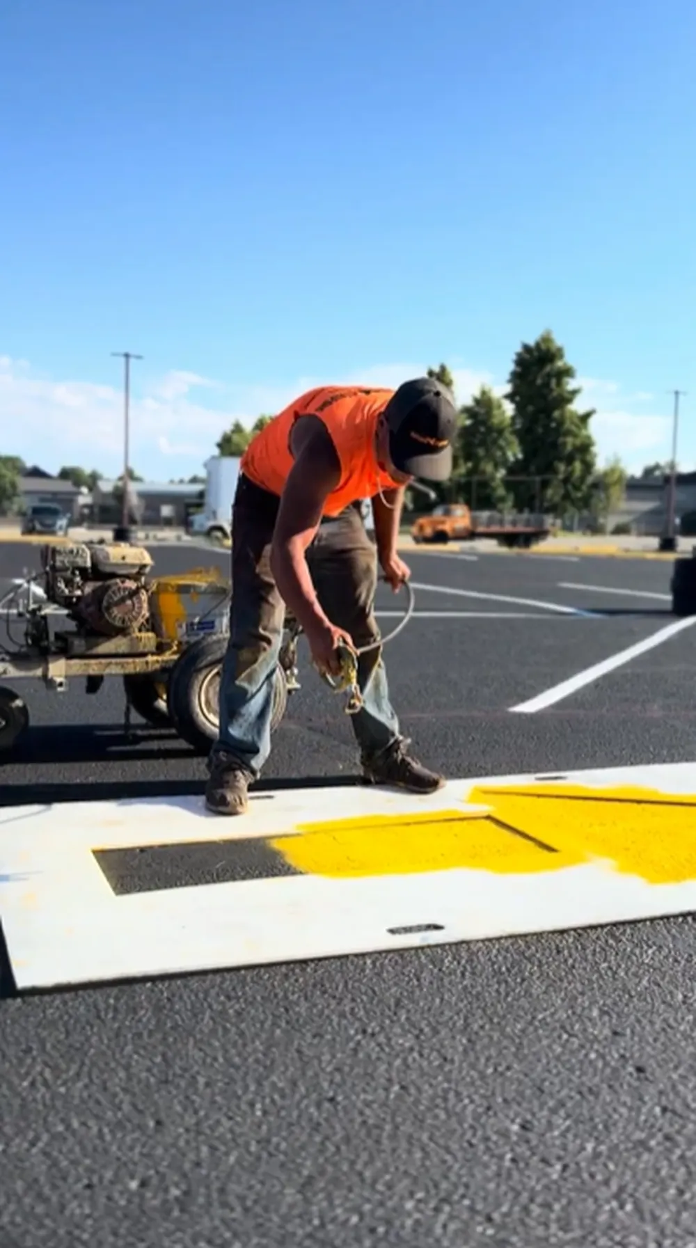 Superior Striping technician spray painting a yellow directional arrow stencil on a freshly sealcoated parking lot in Boise, Idaho