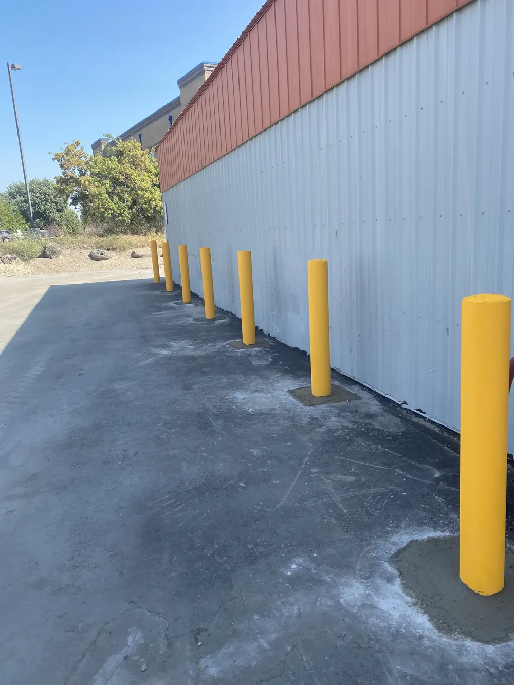 Row of newly installed yellow steel safety bollards along a commercial building wall to prevent vehicle impact, completed by Superior Striping in Treasure Valley.