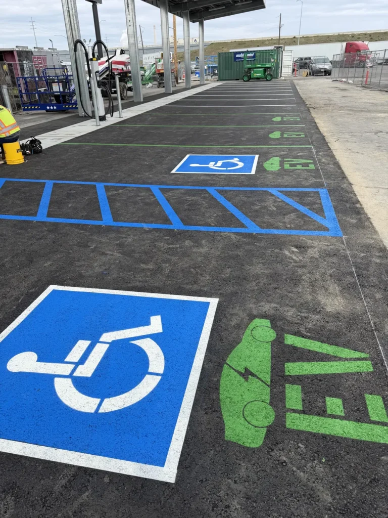 Newly painted vibrant green EV charging station stencils and vivid blue ADA compliant handicap parking markings on fresh asphalt at a commercial site in Boise, Idaho, by Superior Striping.