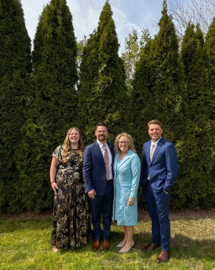 Scott Mitchell, owner of Superior Striping, standing with his family in front of tall evergreen trees, all dressed in formal attire for a family portrait.
