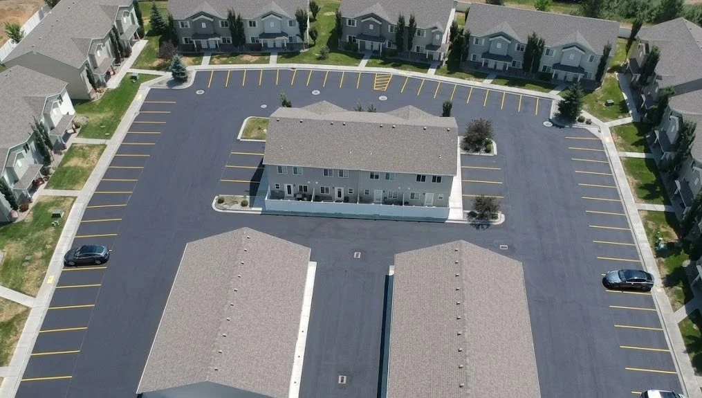 Aerial view of an apartment complex parking lot in Twin Falls, Idaho, featuring fresh black sealcoating and bright yellow parking line striping, professionally completed by Superior Striping.