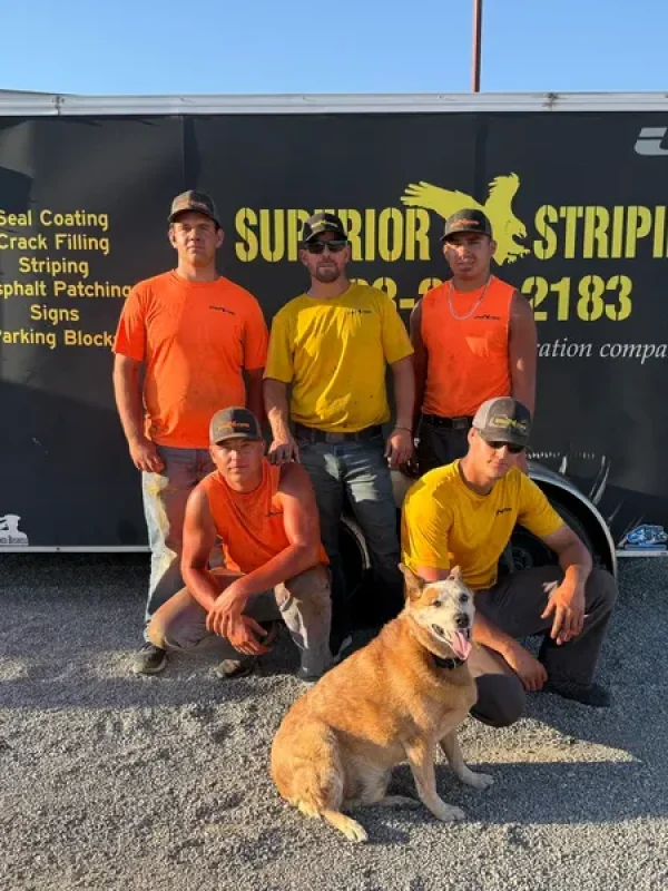 Superior Striping crew posing in front of their service trailer with their dog